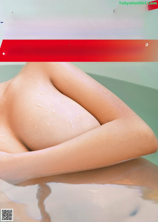 A picture of a woman in a bathtub with water droplets on her breasts.