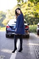 A woman in a blue sweater and black boots standing on the side of a road.