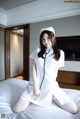 A woman dressed as a nurse sitting on a bed.