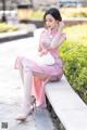 A woman in a pink dress sitting on a stone ledge.