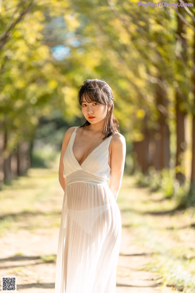 A woman in a white dress standing in a park.