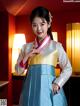 A woman in a blue and white hanbok poses for a picture.