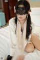 A woman wearing a black mask sitting on a bed.