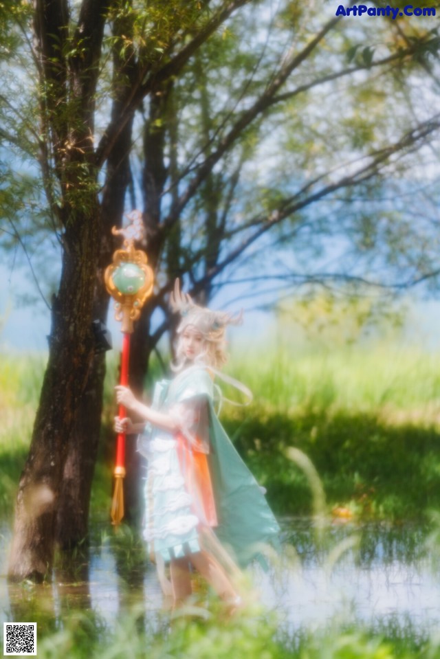 A woman in a green dress holding a wand in the water.