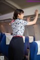 A woman in a blue and white shirt and black skirt on an airplane.