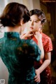 A woman in a red and green cheongsam adjusting her hair.