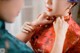 A woman in a red cheongsam is putting on a necklace.