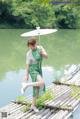 A woman in a green dress holding an umbrella on a wooden bridge.