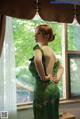 A woman in a green dress standing by a window.