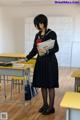 A woman in a school uniform standing in front of a classroom.