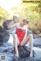 A woman in a red dress sitting on a rock in the water.