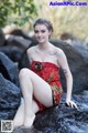 A woman in a red dress sitting on a rock in the water.