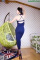 A woman in a blue dress standing next to a hanging chair.