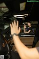 A woman sitting in the driver's seat of a car waving her hand.